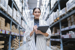 Portrait of asian woman business owner using digital tablet checking amount of stock product inventory on shelf at distribution warehouse factory.logistic business shipping and delivery service